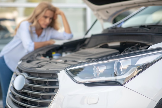 Headlight and open car hood and woman behind