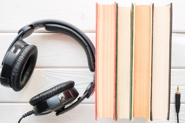 Headphones next to the old books on a white wooden background