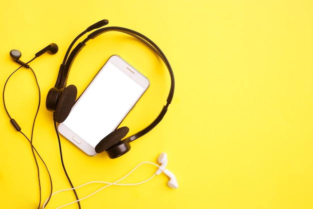 Headphones and smartphone on a yellow table. Clubhouse social media concept. Mock up, copy space, flat lay, top view