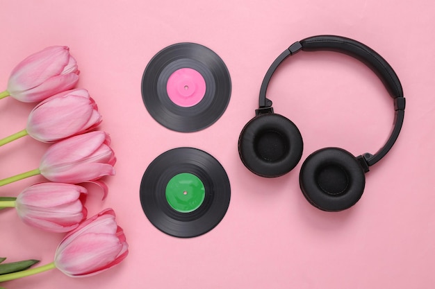 Headphones and vinyl records with pink tulips bouquet on pink background Music day Top view