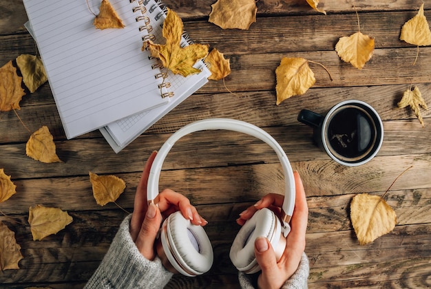 Photo headphones with autumn dry leaves cuo of coffee and notepads on rustic wooden background top view flat lay