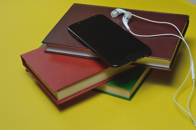 Headphones with books and a smartphone on a yellow background.