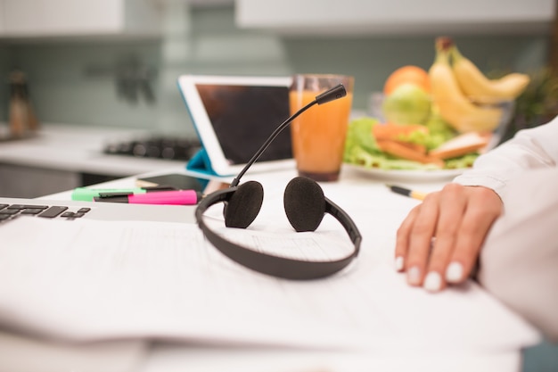 Headphones with a headset are on the table. Close-up workplace in the kitchen. A woman works from home.