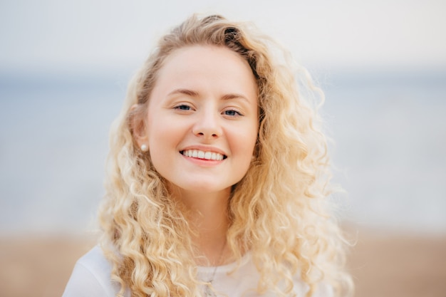 Headshot of beautiful woman with friendly smile, has healthy skin, being in good mood after unforgettable rest in resort.