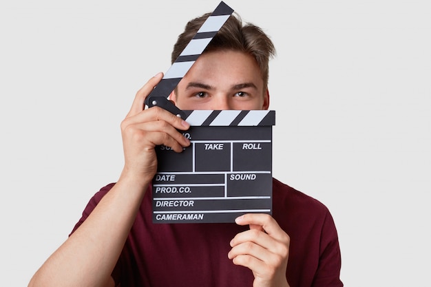 Headshot of handsome man hides face with clapper board