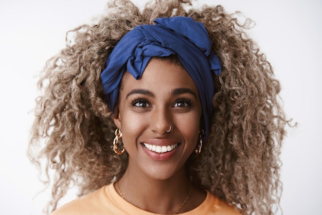 Headshot lively and enthusiastic carefree stylish africanamerican curlyhaired blond female in blue hipster headband smiling toothy look with happy sincere expression standing entertained