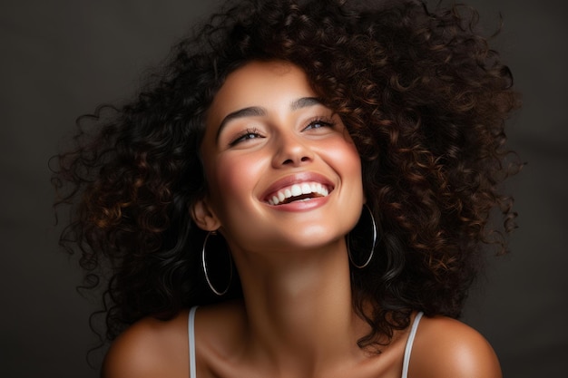 Headshot portrait of laughing cheerful girl with curly hairstyle and white toothy smile on grey background