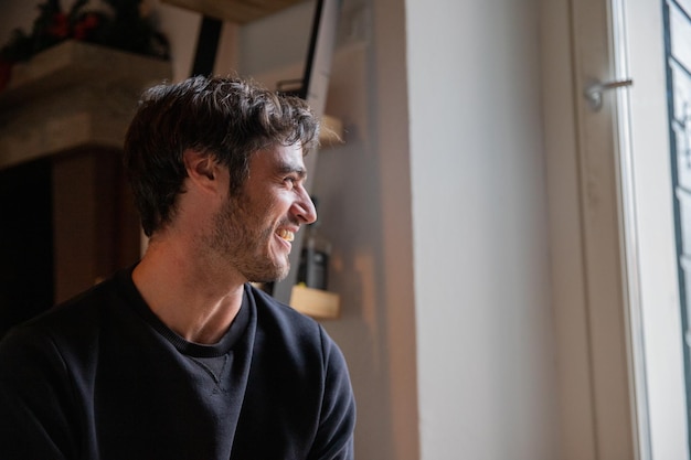 Headshot of a smiling young caucasian man in his 30s looking at the window in his room