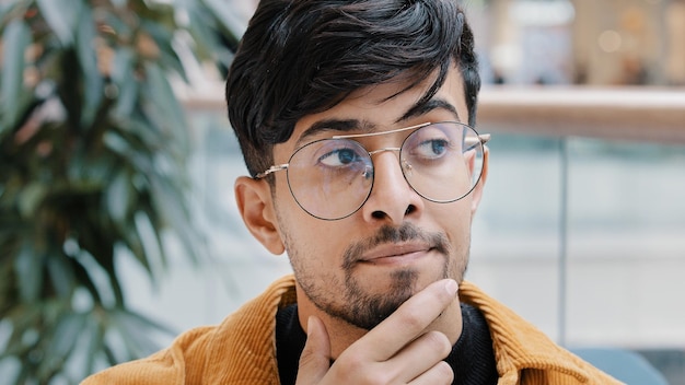 Headshot young pensive thoughtful indian man holding hand on chin thinking deep