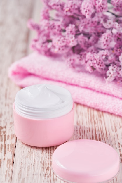 Healing herbal cosmetic cream, hygienic skin care product or relaxing makeup mask in a pink jar with a towel on a wooden table.