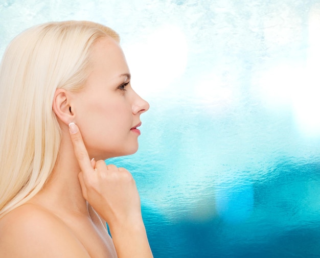 health and beauty concept - close up of clean face of beautiful young woman pointing finger to ear