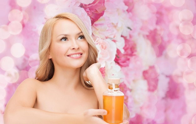 health and beauty concept - happy woman with oil bottle