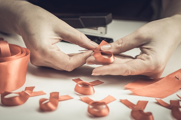 Health care and medicine concept. AIDS awareness. Female hands make red awareness ribbons with a red ribbon and a stapler. World aids day.