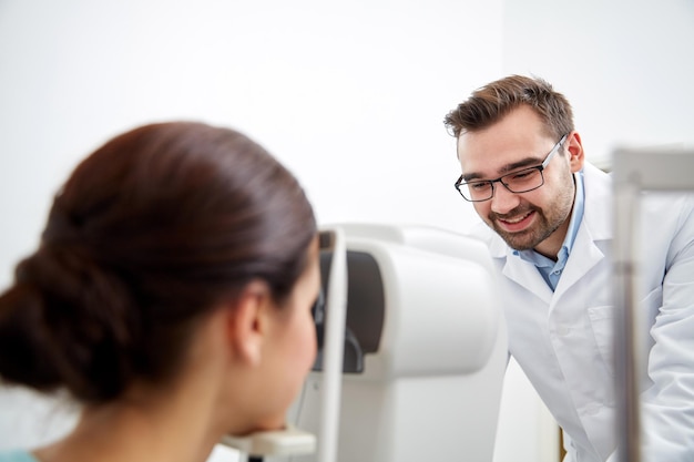 health care, medicine, people, eyesight and technology concept - optometrist with non contact tonometer checking patient intraocular pressure at eye clinic or optics store