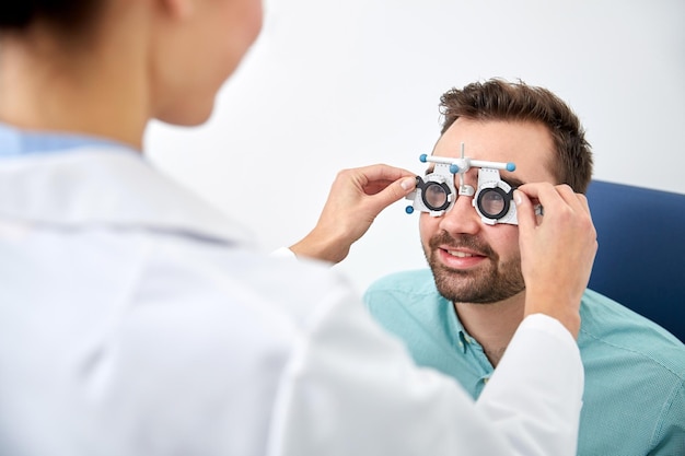 health care, medicine, people, eyesight and technology concept - optometrist with trial frame checking patient vision at eye clinic or optics store