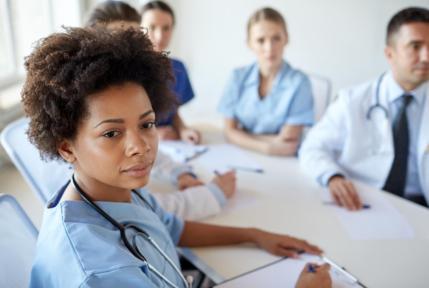 health care, profession, people and medicine concept - african american female doctor or nurse over group of medics meeting at hospital