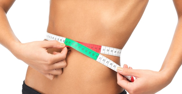 health, dieting and fitness concept - close up of woman measuring her waist with measuring tape