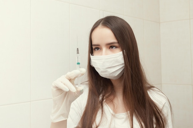 Health and medicine Girl doctor in a mask and gloves holds a syringe with a vaccine