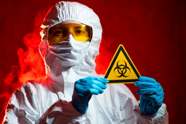 Health, medicine and pandemic concept - female doctor holding boihazard caution sign