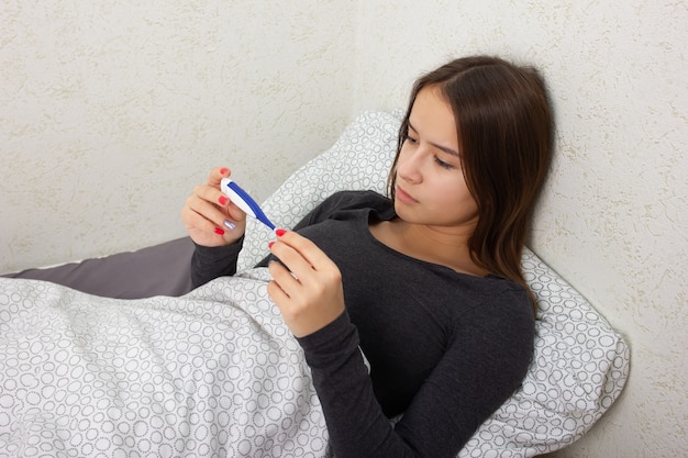 Health and medicine. A young girl is sick at home in bed, holds a thermometer.