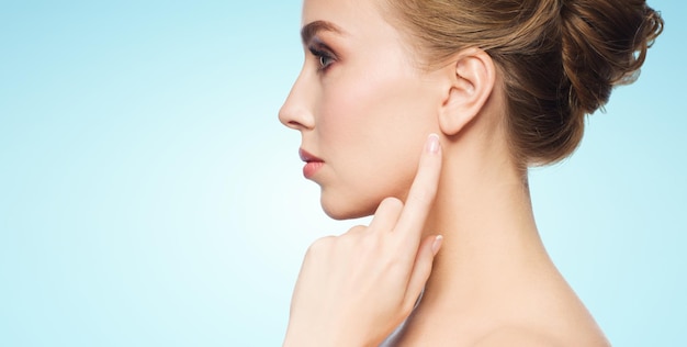 health, people and beauty concept - beautiful young woman pointing finger to her ear over blue background