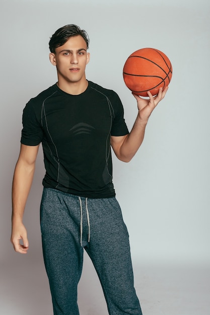 Photo health, people, sport and lifestyle concept - real player. handsome young smiling man carrying a basketball ball and looking at camera while standing against grey background