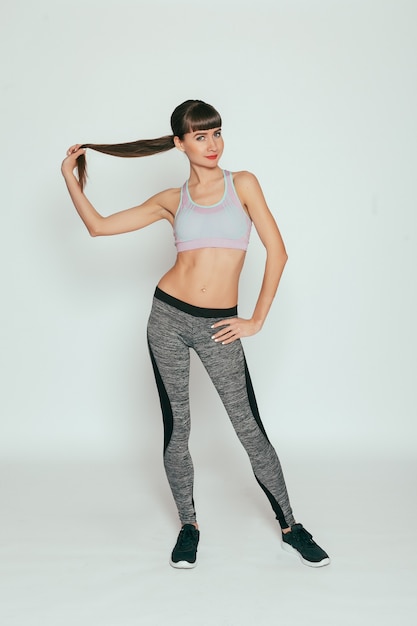 Health, people, Sport and lifestyle concept - Young happy fitness girl with sporty body at studio on a gray surface