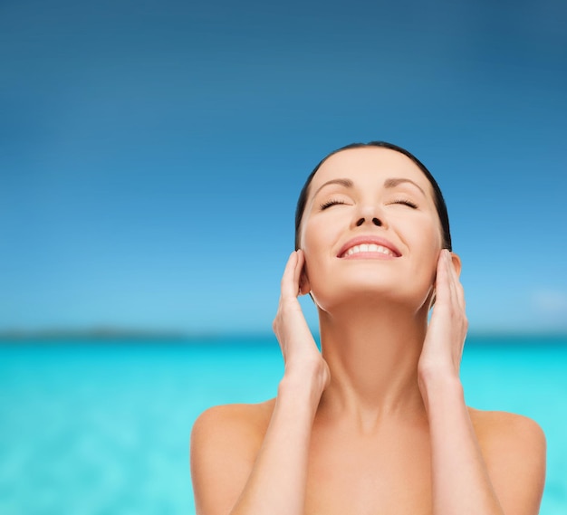 health, spa and beauty concept - clean face and hands of beautiful smiling woman with closed eyes