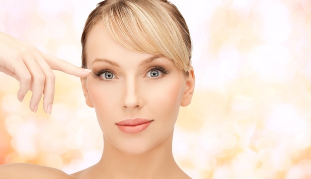 health, spa and beauty concept - face of beautiful woman touching her eye area