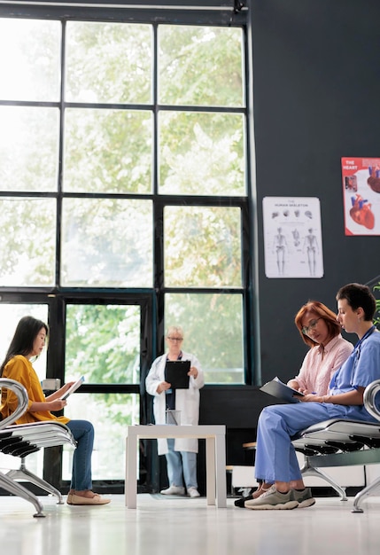 Health specialist discussing with senior woman in hospital waiting room, filling report papers explaining healthcare treatment. Nurse doing checkup examination with asian patient in lobby.