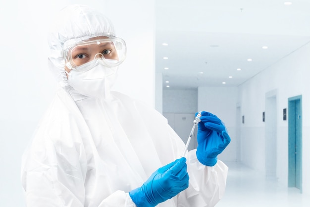 Health worker woman with a protective suit and gloves holding covid 19 vaccines on the hospital