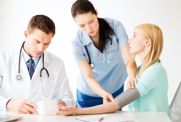 healthcare and medical concept - doctor and nurse with patient measuring blood pressure in hospital