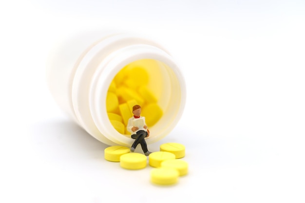 Healthcare Medical and Information Concept Closeup of businesswoman miniature figure sitting and reading book on bottle of yellow pills on white background