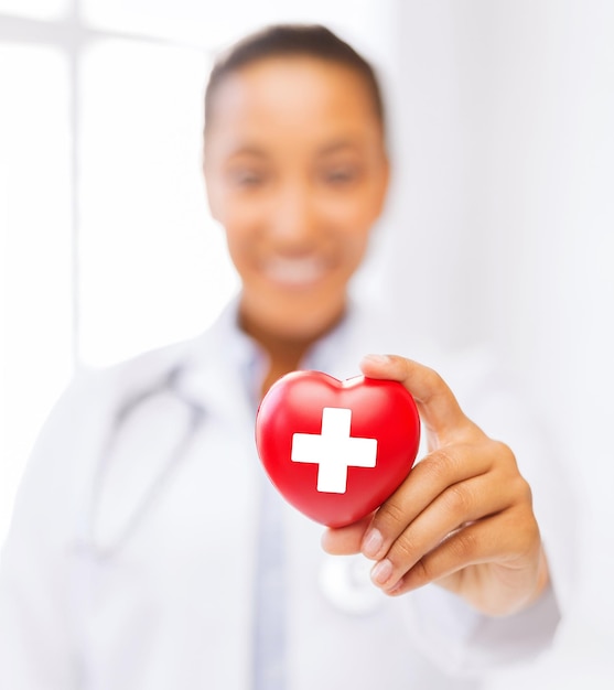 healthcare and medicine concept - female african american doctor holding heart with red cross symbol