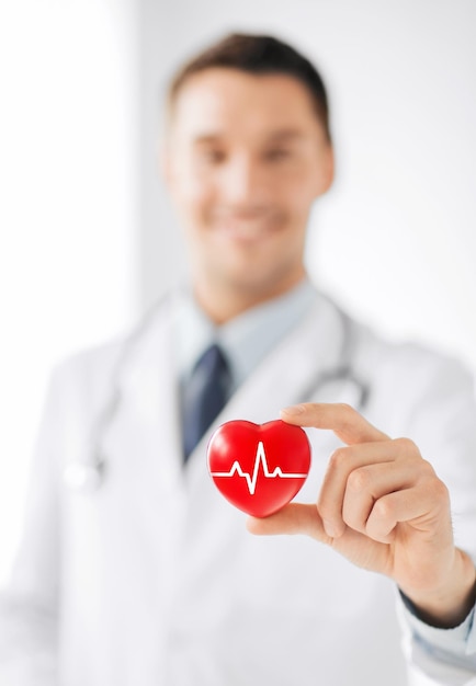 healthcare and medicine concept - male doctor holding red heart with ecg line