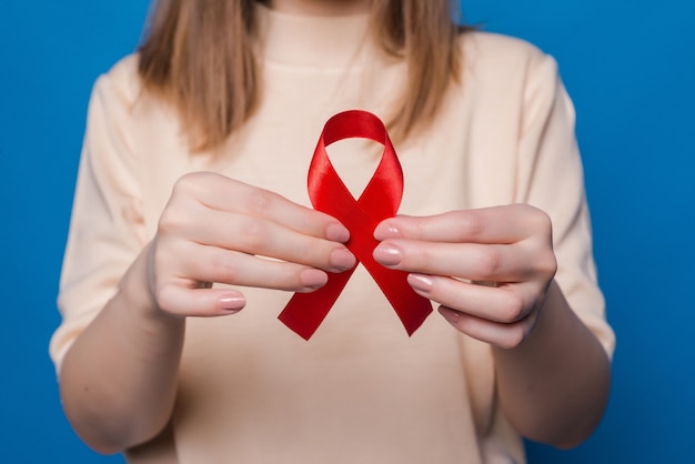 Healthcare and medicine concept. Young girl hands holding red breast cancer awareness ribbon on blue wall