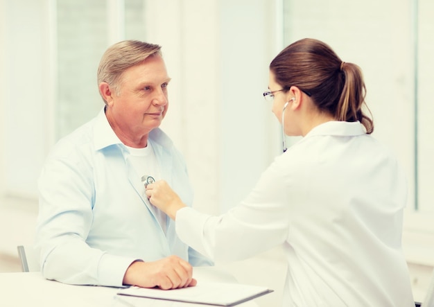 healthcare, medicine and elderly concept - female doctor or nurse with old man listening to heart beat