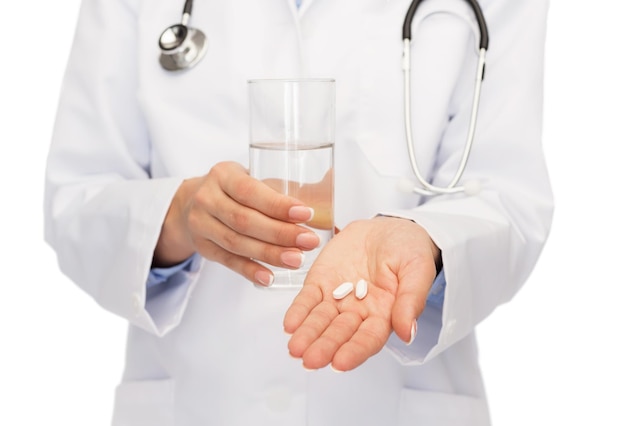 healthcare, medicine and pharmacy concept - close up of doctor with stethoscope offering pills and water