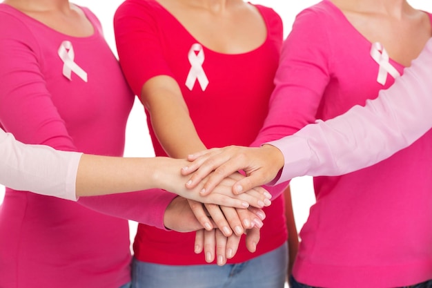 healthcare, people, gesture and medicine concept - close up of women in blank shirts with pink breast cancer awareness ribbons putting hands on top over white background