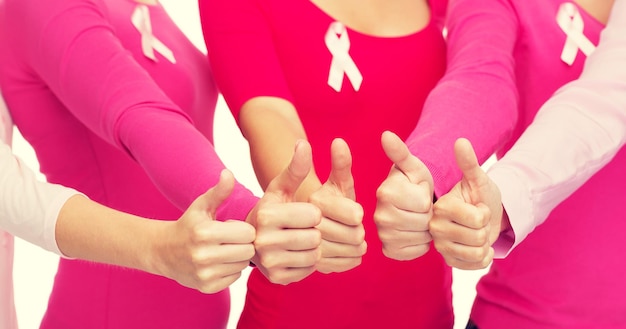 healthcare, people, gesture and medicine concept - close up of women in blank shirts with pink breast cancer awareness ribbons showing thumbs up over white background