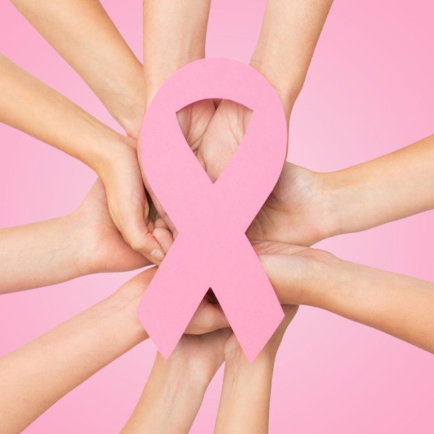 healthcare, people and medicine concept - close up of women hands with paper cancer awareness symbol over pink background