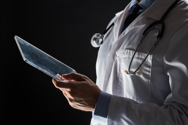 healthcare, people, technology and medicine concept - close up of male doctor in white coat with stethoscope and tablet pc computer over black background