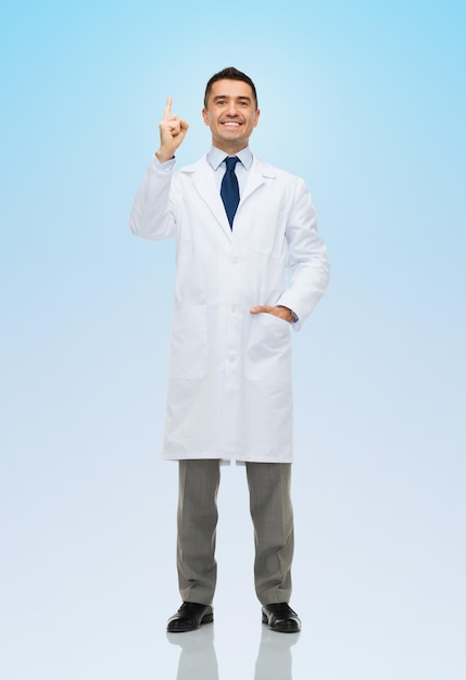 healthcare, profession, people and medicine concept - smiling male doctor in white coat pointing finger up over blue background