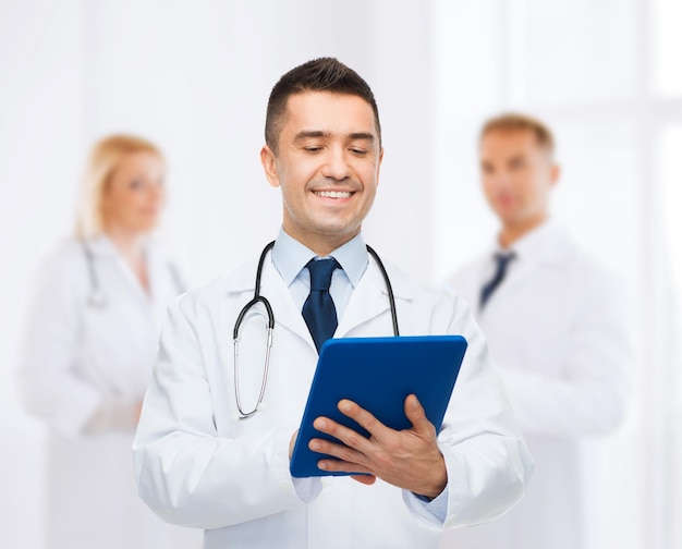 healthcare, profession, people and medicine concept - smiling male doctor in white coat with tablet pc over group of medics at hospital background