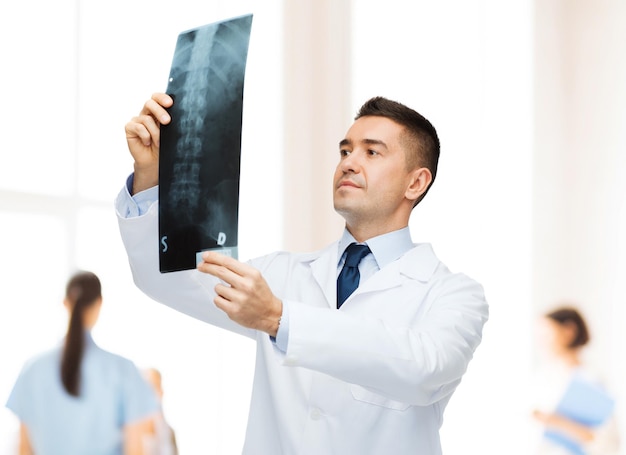 healthcare, roentgen, people and medicine concept - male doctor in white coat looking at x-ray over group of medics at hospital background