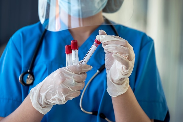 Healthcare worker in protective gloves holds a test tube with blood, receiving a positive test for coronavirus