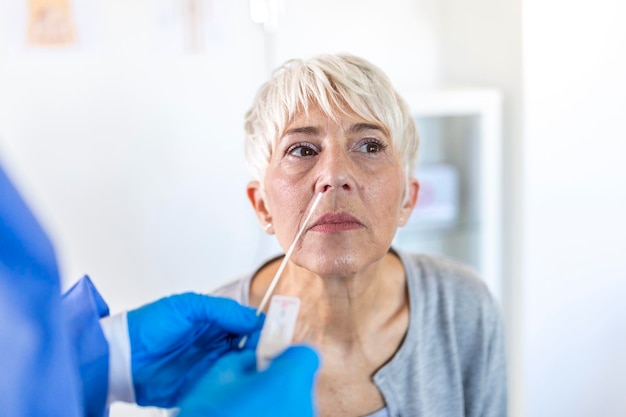 Healthcare worker with protective equipment performs coronavirus swab on mature woman.Nose swab for Covid-19.