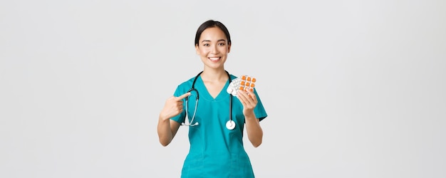 Healthcare workers, preventing virus, quarantine campaign concept. Smiling friendly female physician, nurse in scrubs pointing finger at vitamins or pills, showing medication, white background