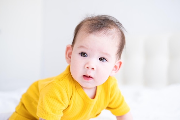 healthy asian baby girl 5 months in yellow bodysuit on bed on white bedding