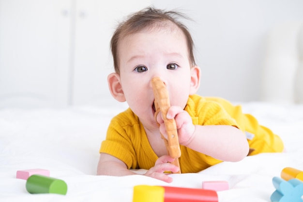 healthy asian baby girl in yellow bodysuit playing with wooden toys on white bedding